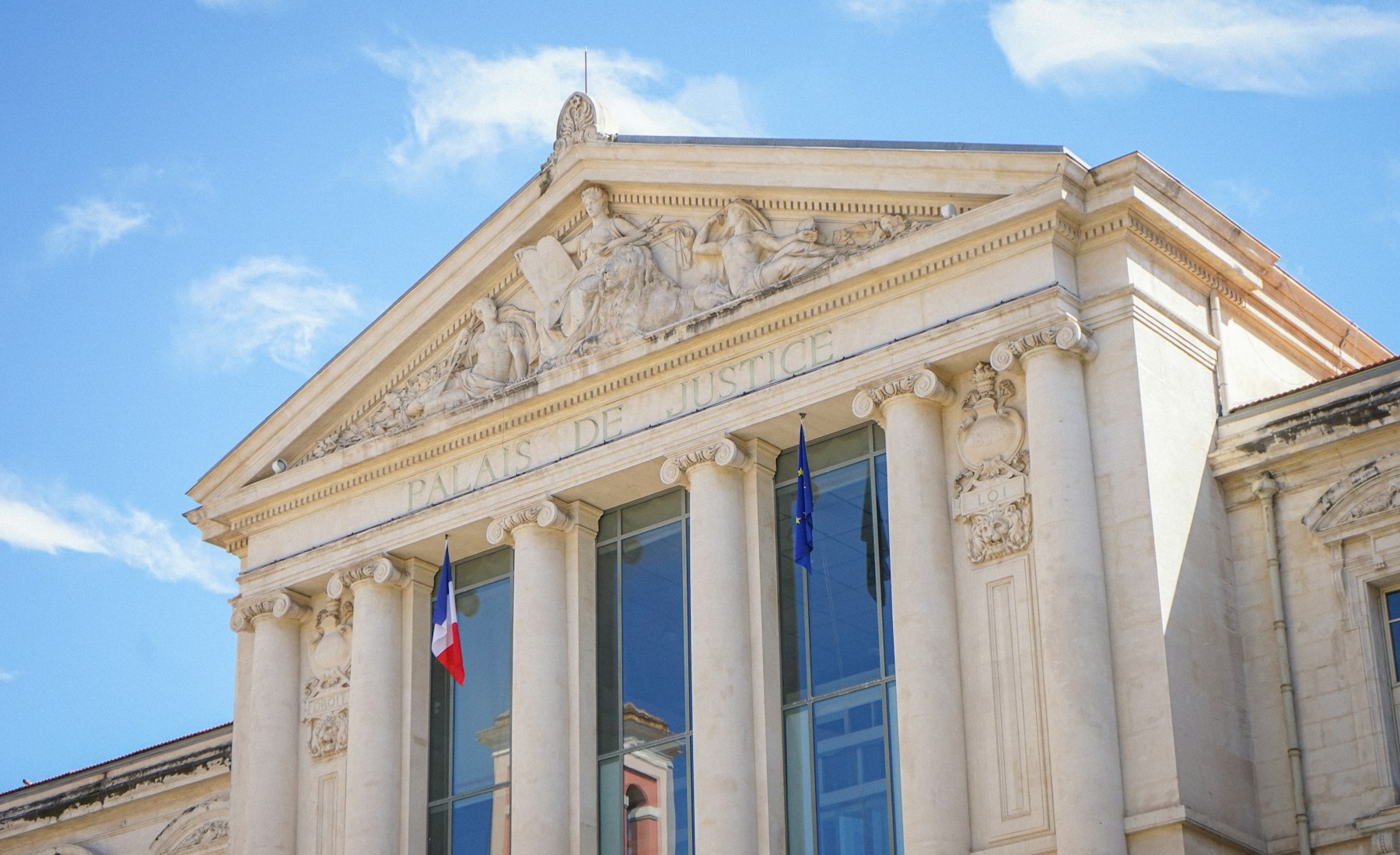 Fronton d’un palais de justice, colonnes de pierre claire et drapeaux.